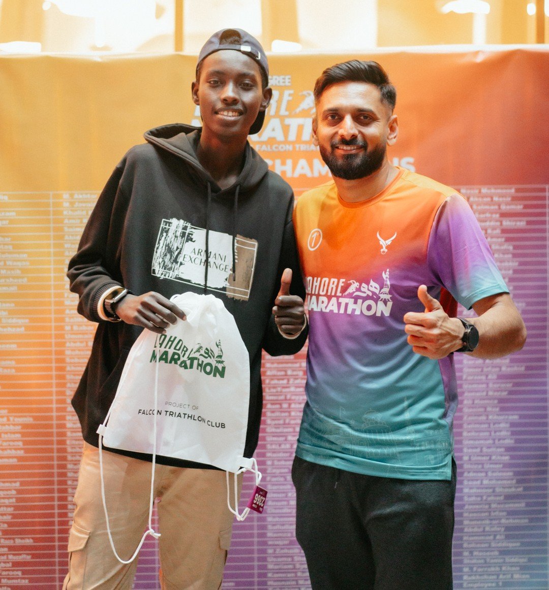 A race winner and a club member holding a Falcon Triathlon Club race bag in front of the champions wall